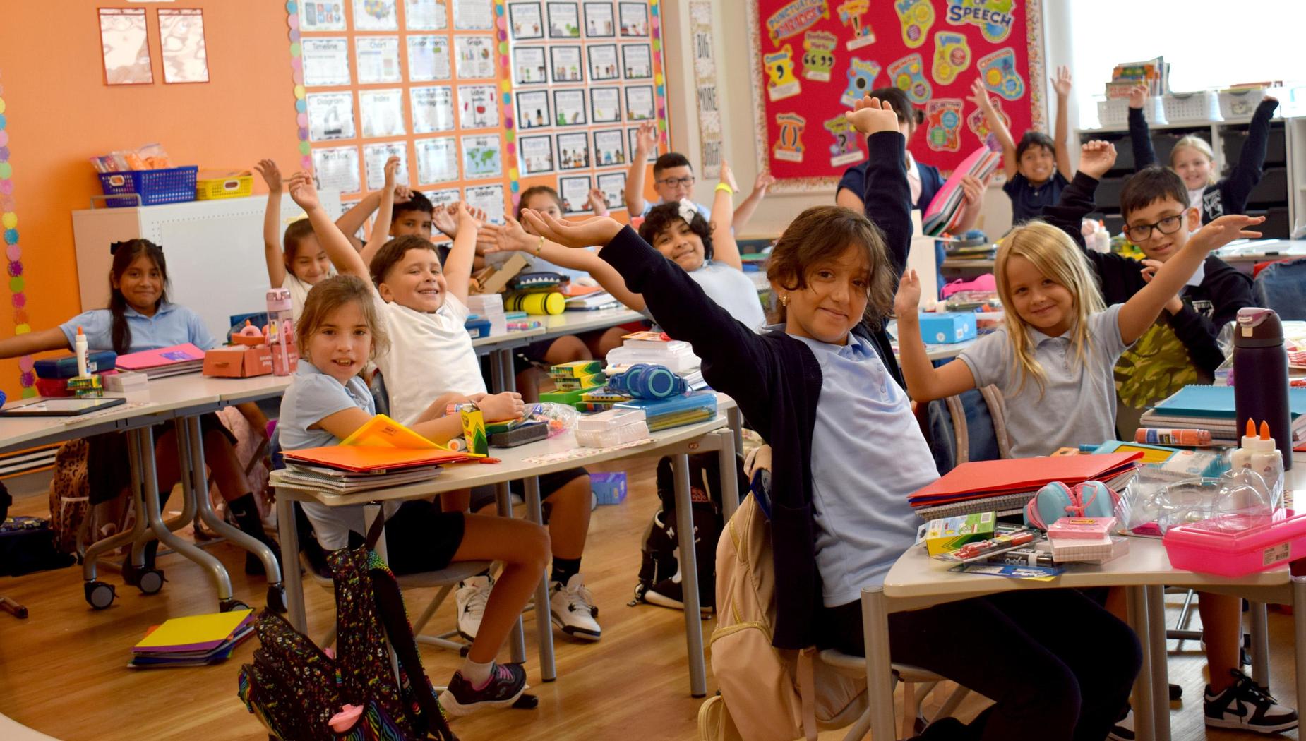 A classroom filled with children raising their arms enthusiastically.