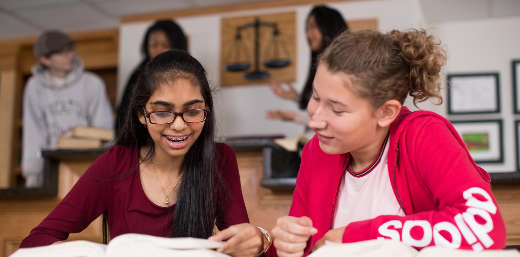 Two students smile while looking at a book in the HSC Courtroom