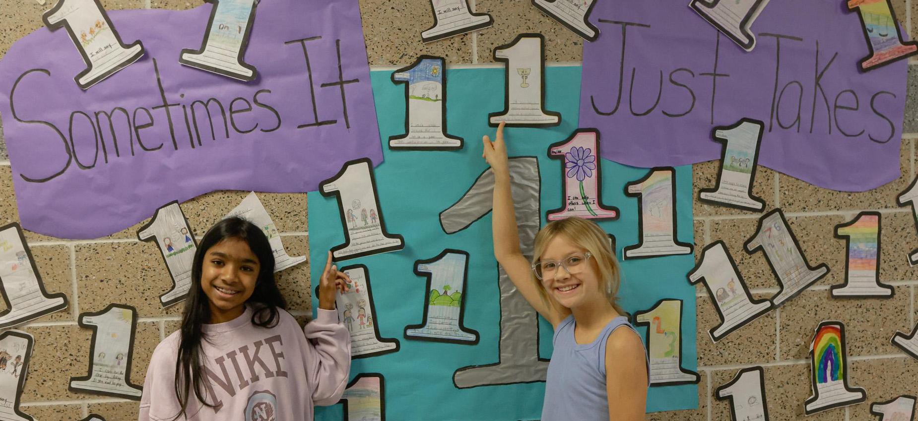 Two children pointing at a colorful wall with the number '1' and a motivational phrase.
