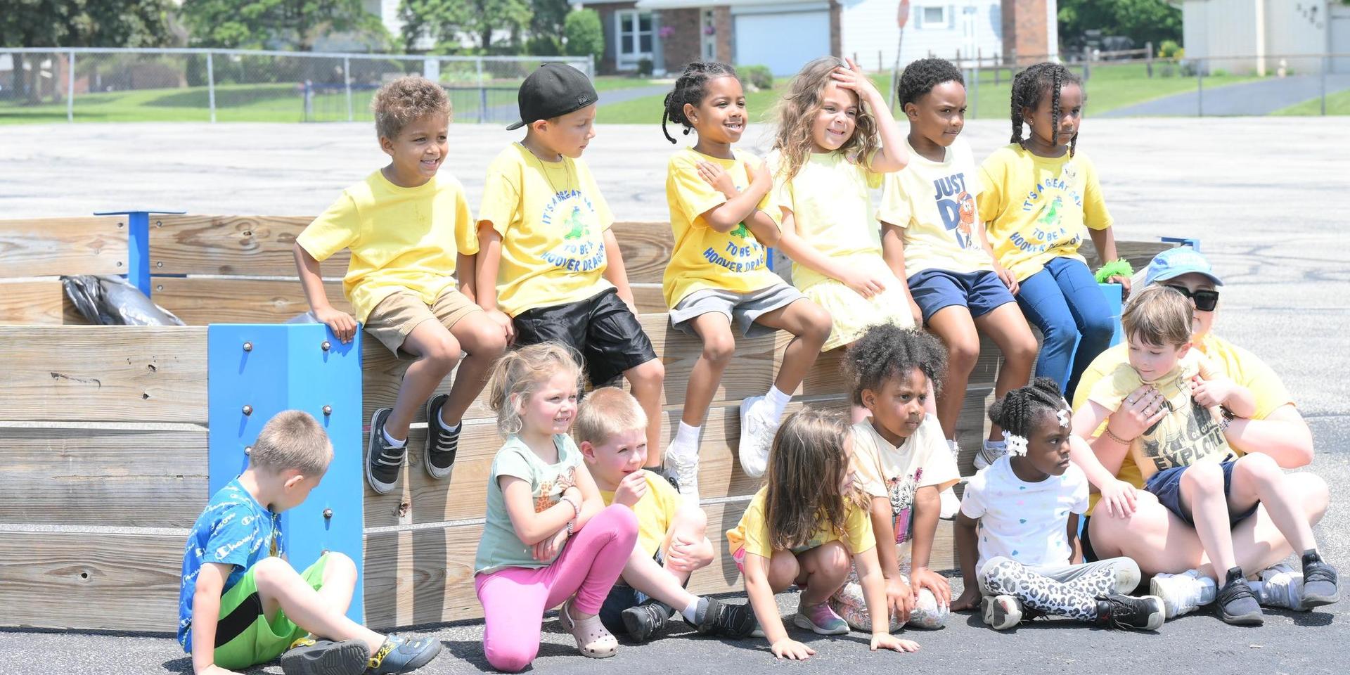 Diverse group of children seated on a wooden structure, posing for a group photo outdoors.