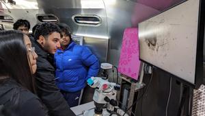 Students engaging with a microscope inside the BIOBUS, observing specimens on a screen.