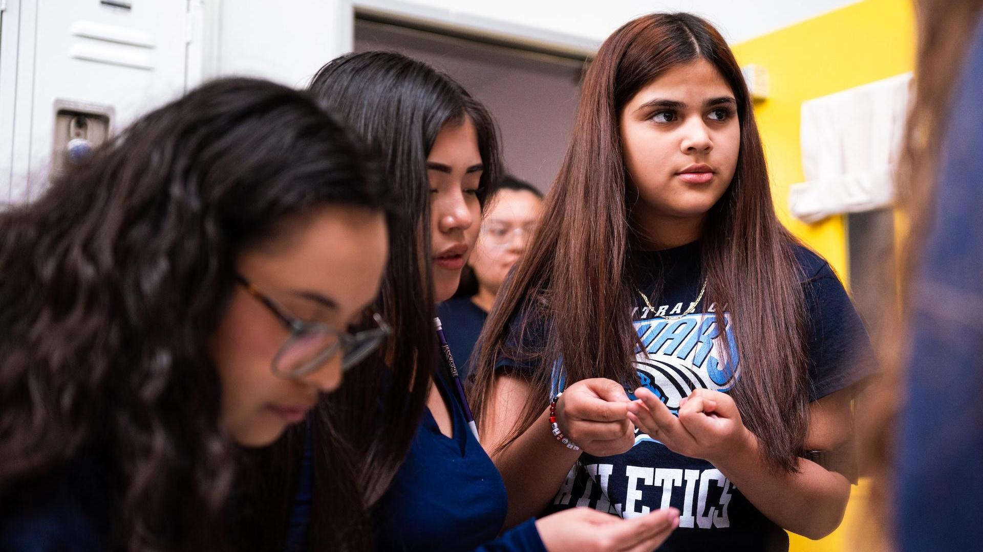 Three girls discussing something while standing near lockers.