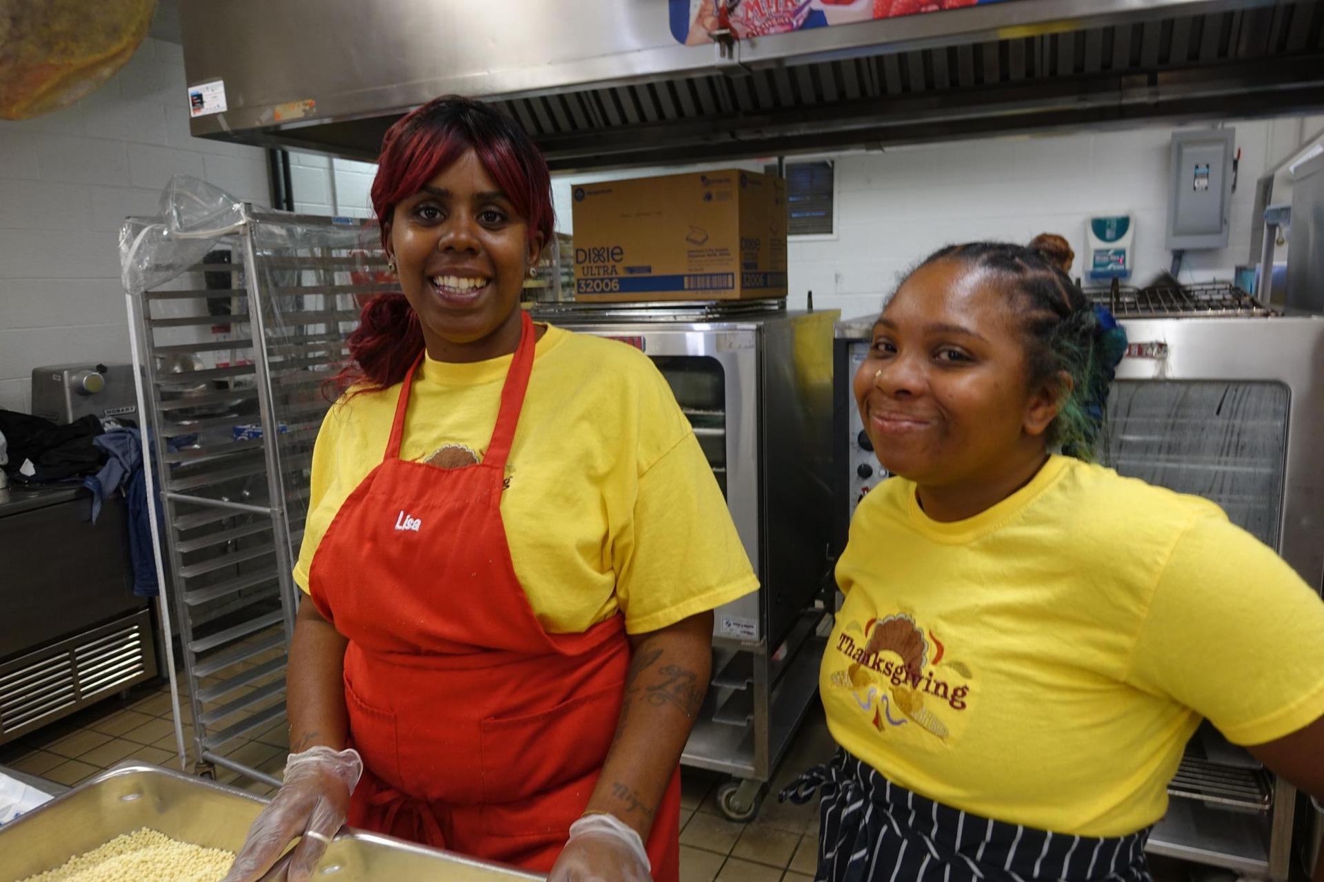 Two women in yellow shirts smiling in a kitchen setting.