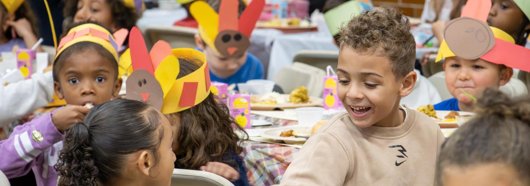Children in colorful hats enjoy a festive meal at a celebration.