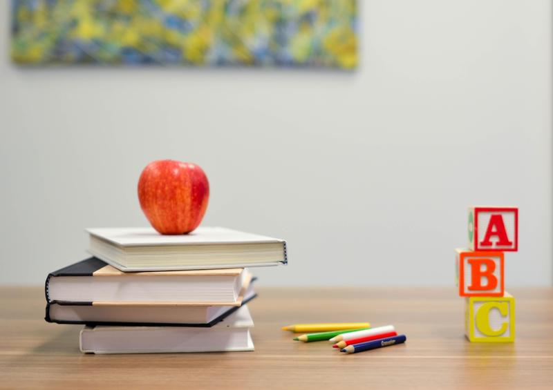 Red apple on a stack of books next to colored pencils and blocks spelling A, B, C.