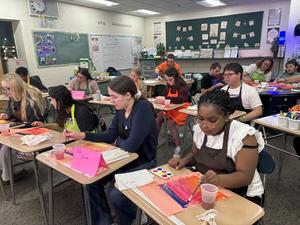 Students engaged in painting activities at desks in a colorful art classroom.