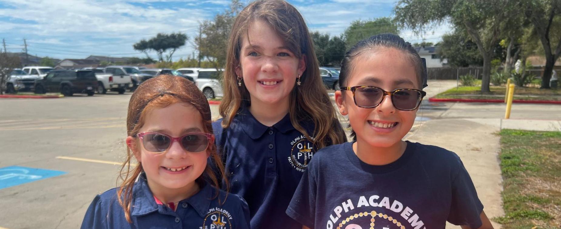 Three children wearing sunglasses and school uniforms, holding a box of Gansito snacks.