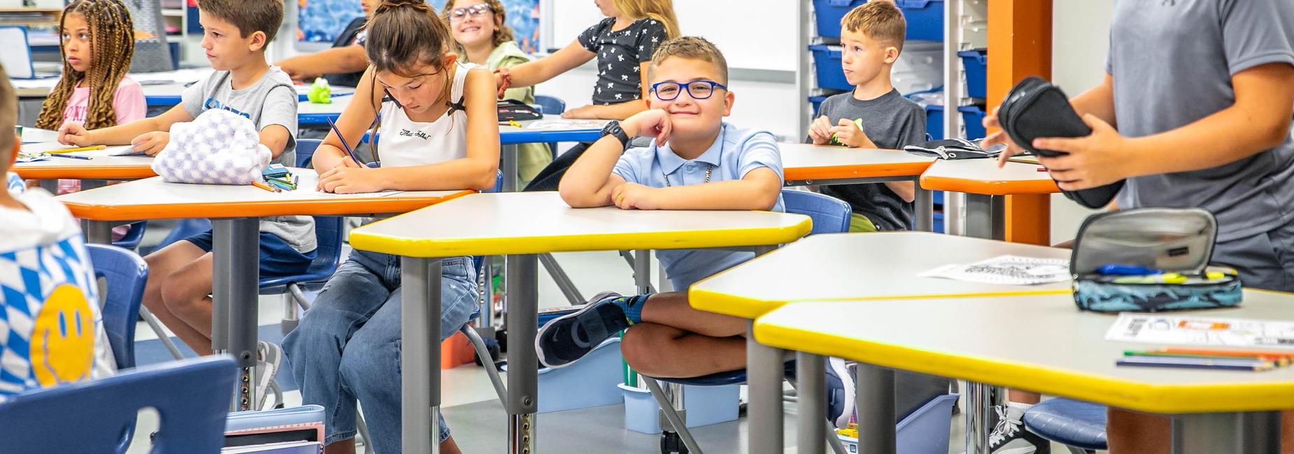 Students engaged in classroom activities, with one boy smiling at the camera.