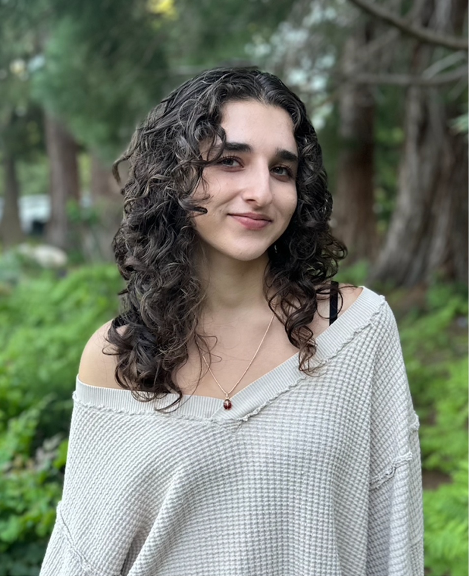 Young woman with curly hair smiling in a natural setting.