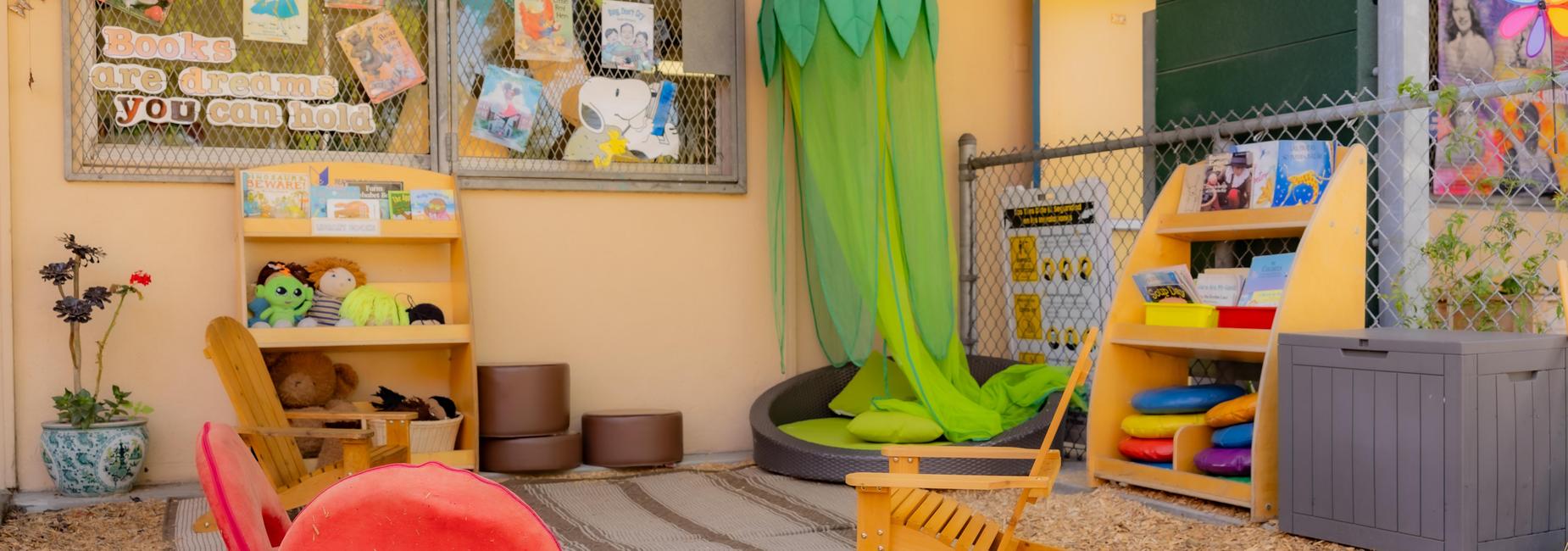 A vibrant outdoor reading corner with books, soft seating, and a green canopy.