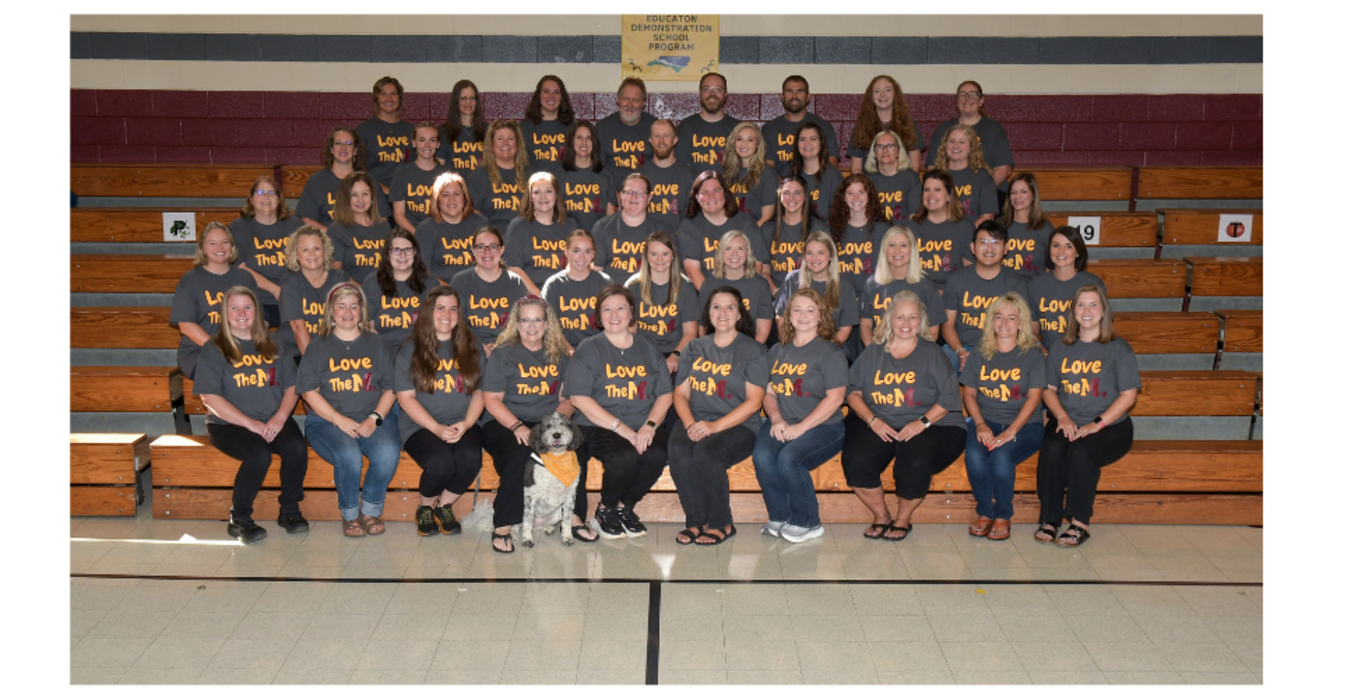 Larger group of people in matching shirts seated on bleachers with a dog.