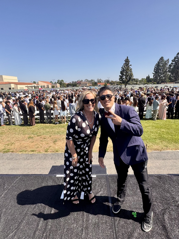 Two smiling people pose together in front of a large crowd at an outdoor event.