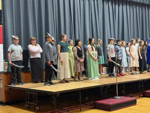 A group of students in costumes performs on stage, showcasing a play or presentation.