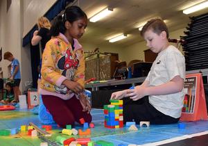 Girl and boy collaborate to build with colorful blocks on the floor.