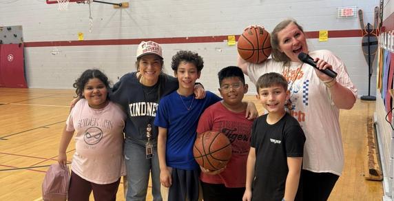 students and teachers holding basketballs smiling in a gym