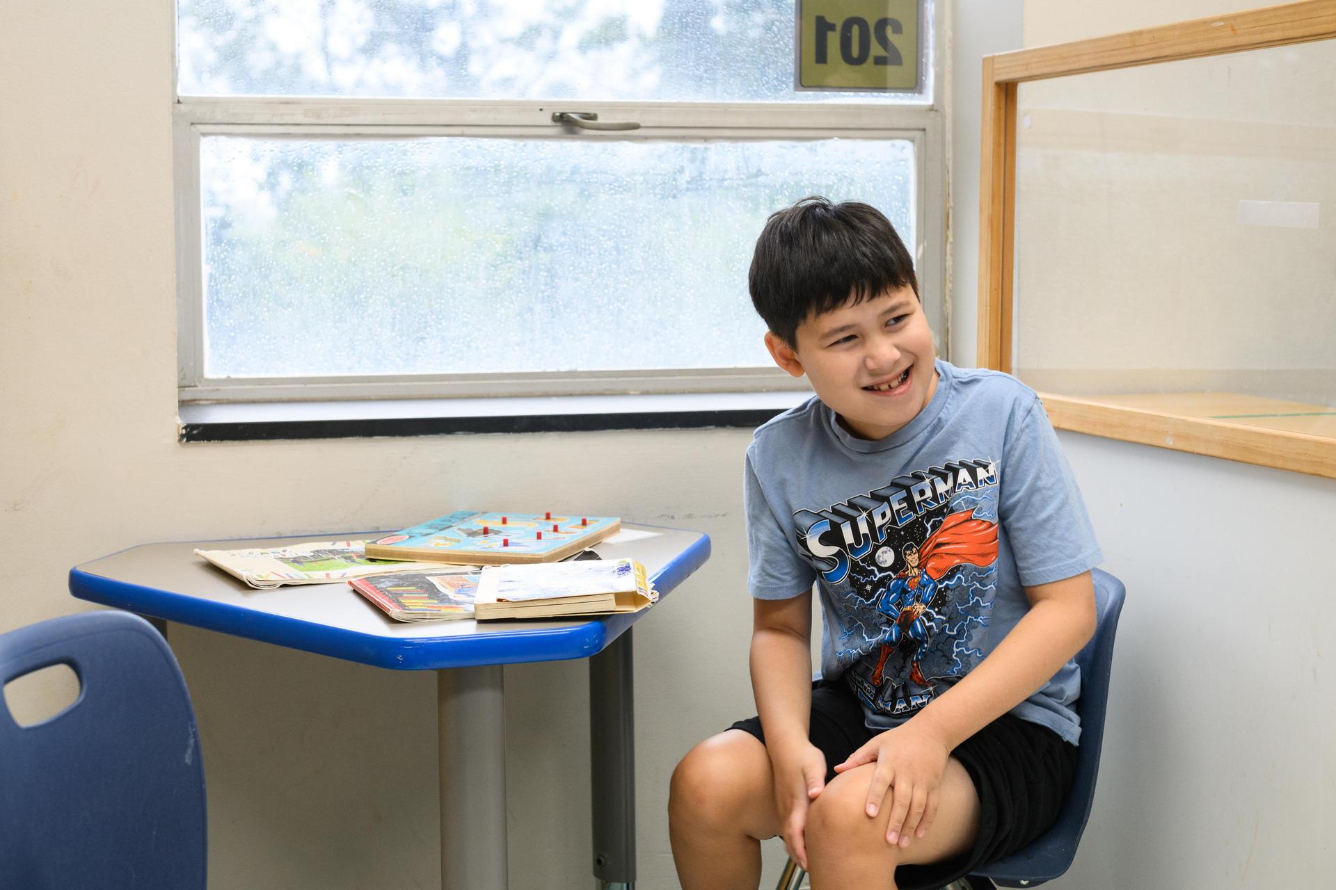 Boy sitting at desk and laughing. 