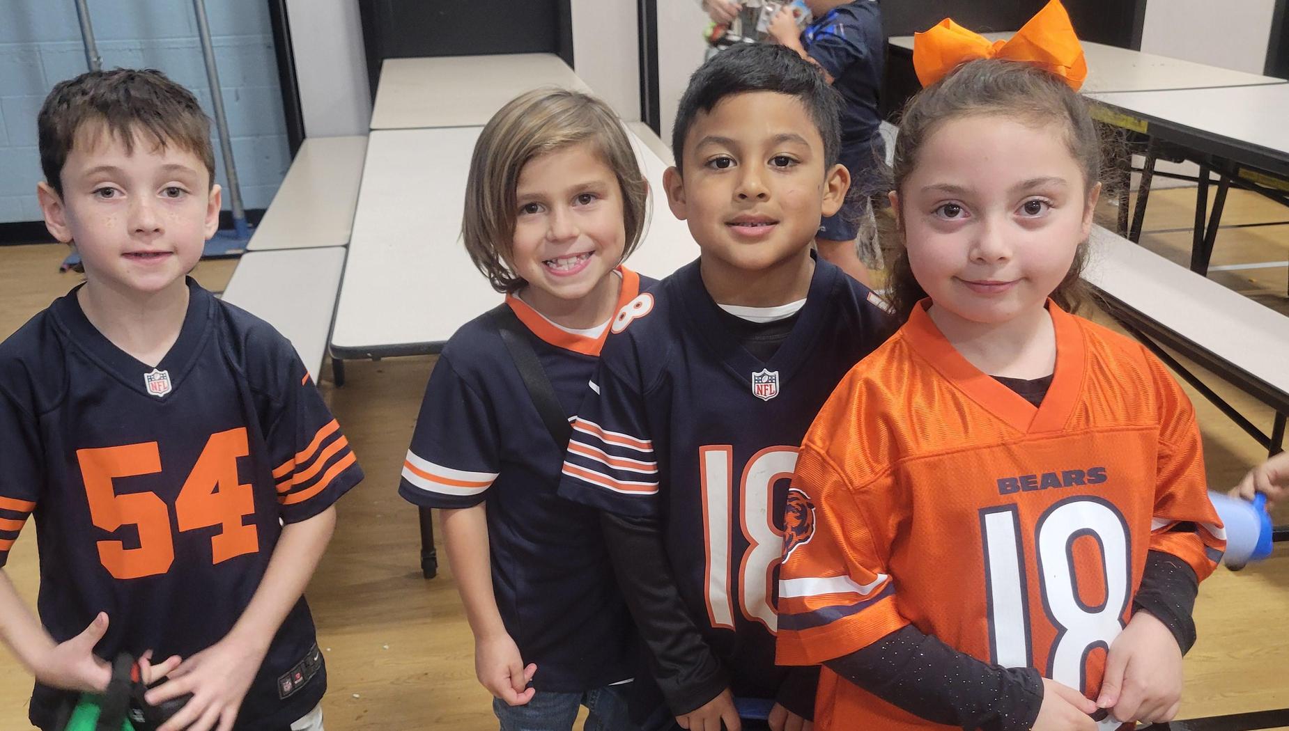 Four children wearing different football jerseys and smiling together.