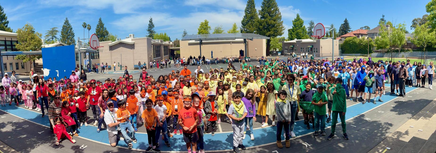 Roosevelt school, wearing rainbow colored shirts, gathers in a playground under blue skies.