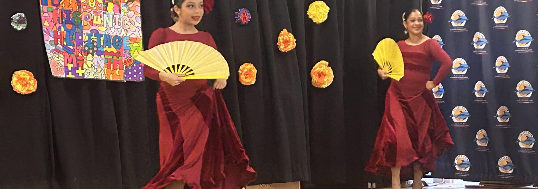 Dancer in red dress performing with a yellow fan, colorful backdrop with flowers.