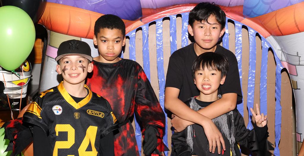 4 boys wearing Halloween costumes standing in front of a display.