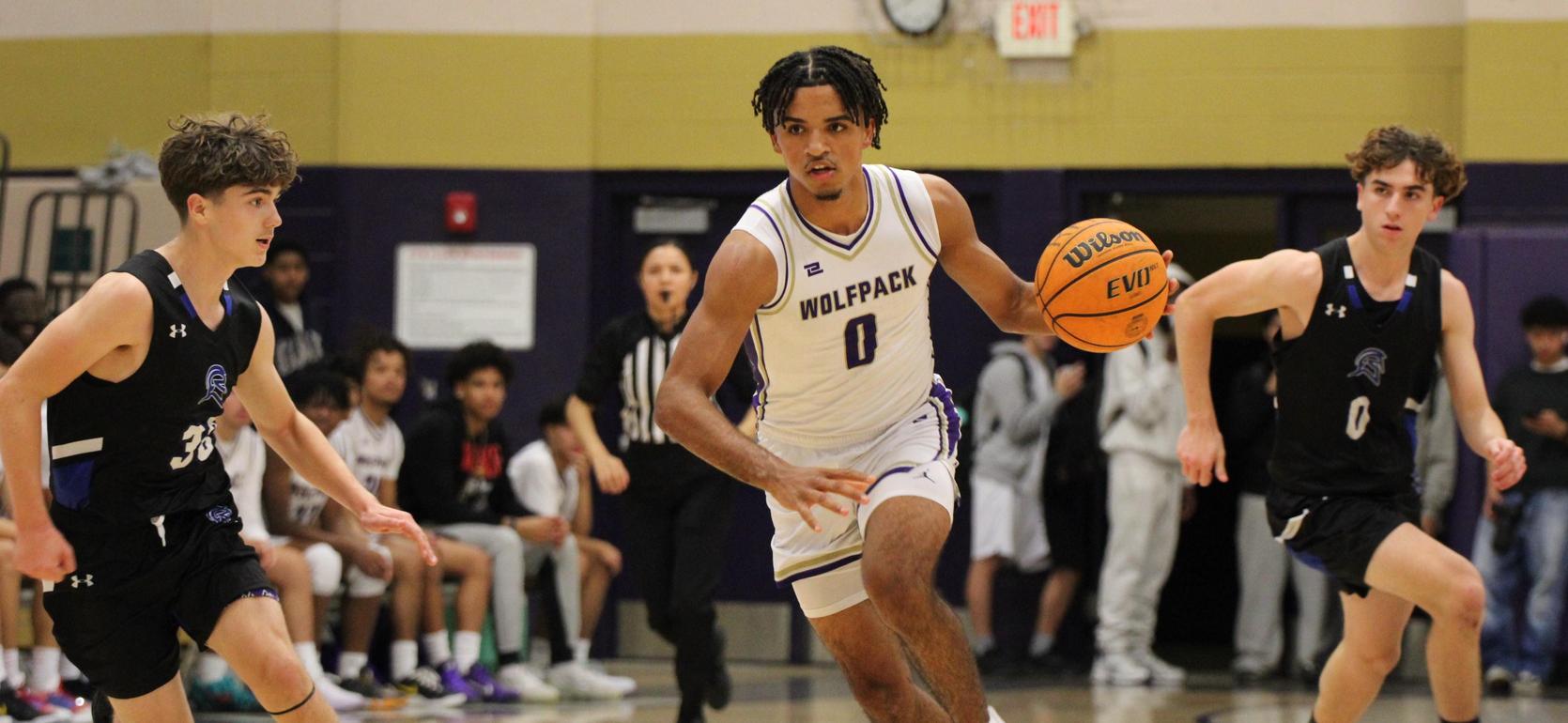 Basketball player dribbling the ball between two opponents during a game.