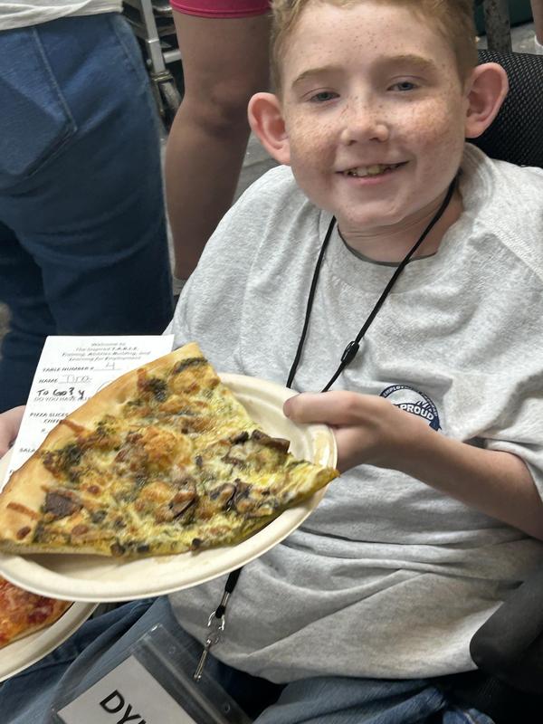 PEP students displays a slice of pizza he helped make