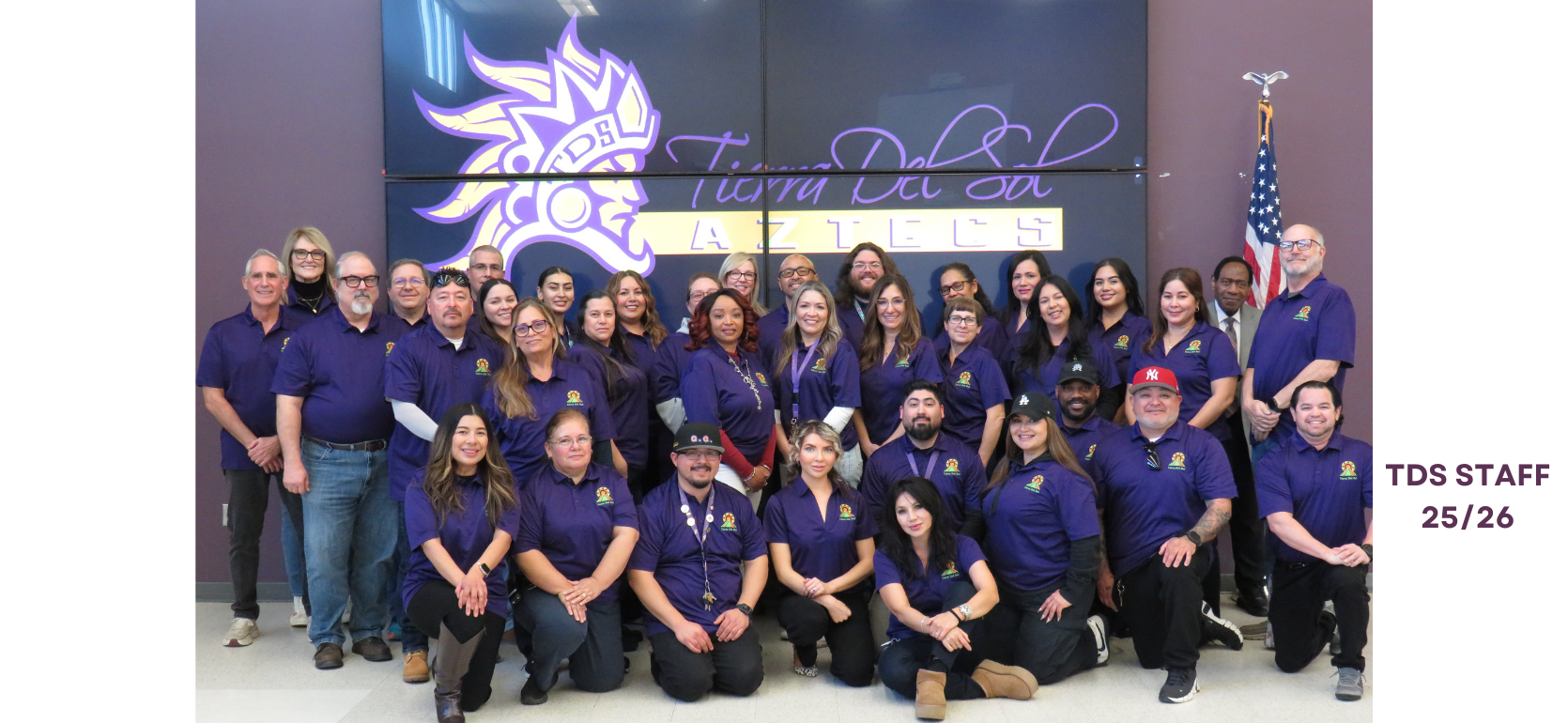 Group photo of TDS staff members wearing purple shirts, smiling in a school setting.