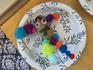 A potato character adorned with colorful pom-poms, arranged on a paper plate.
