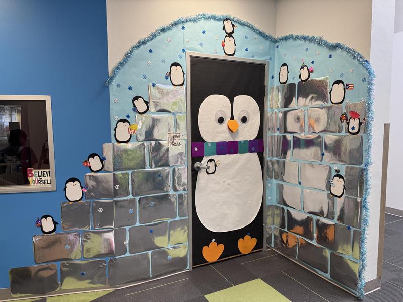 Metallic paper is stacked into a brick shape with a large penguin looking through the door, and smaller penguins all around.