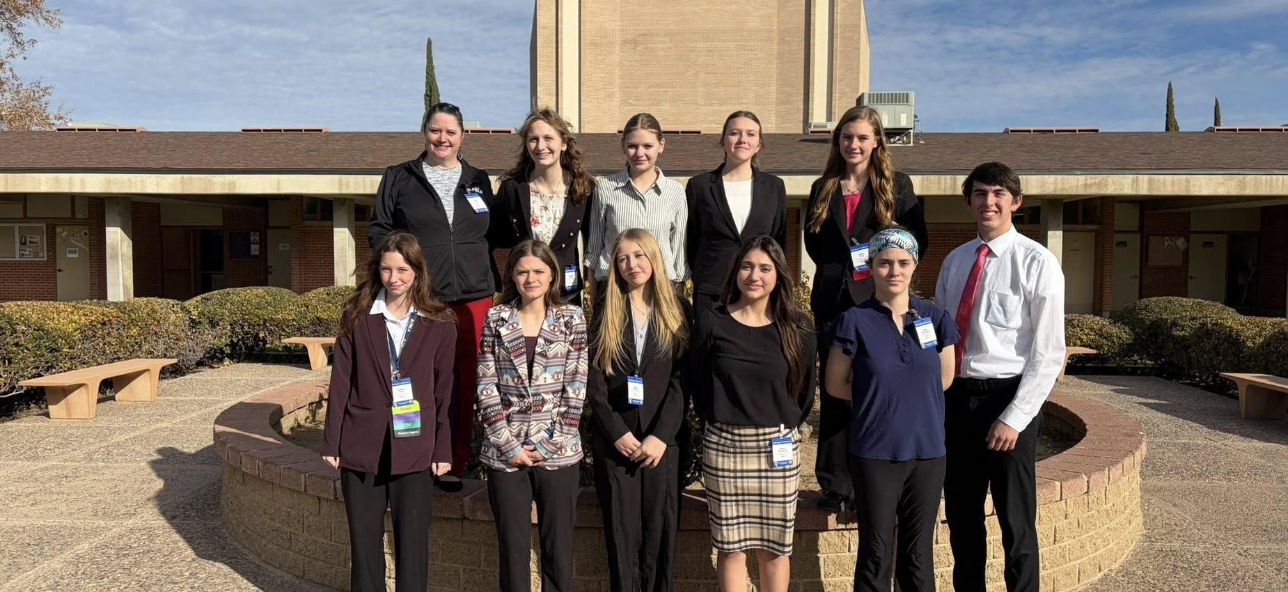 A diverse group of twelve individuals standing in front of a large building, smiling for the camera.
