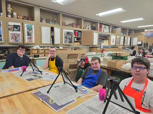 Group of art students seated at tables with easels, ready to paint.
