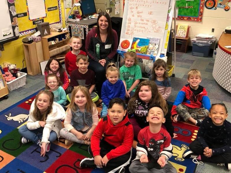 students and teacher pose together on their classroom rug