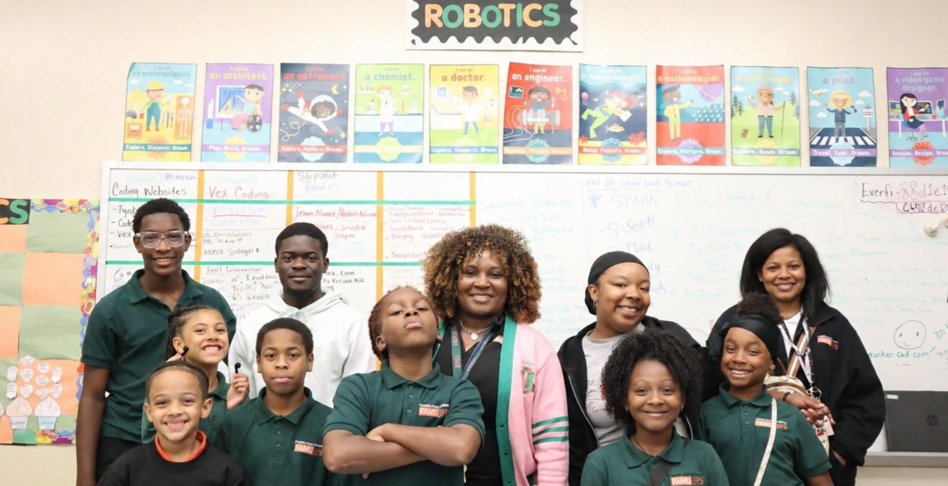 Group of students and teachers posing in a classroom with a robotics theme.