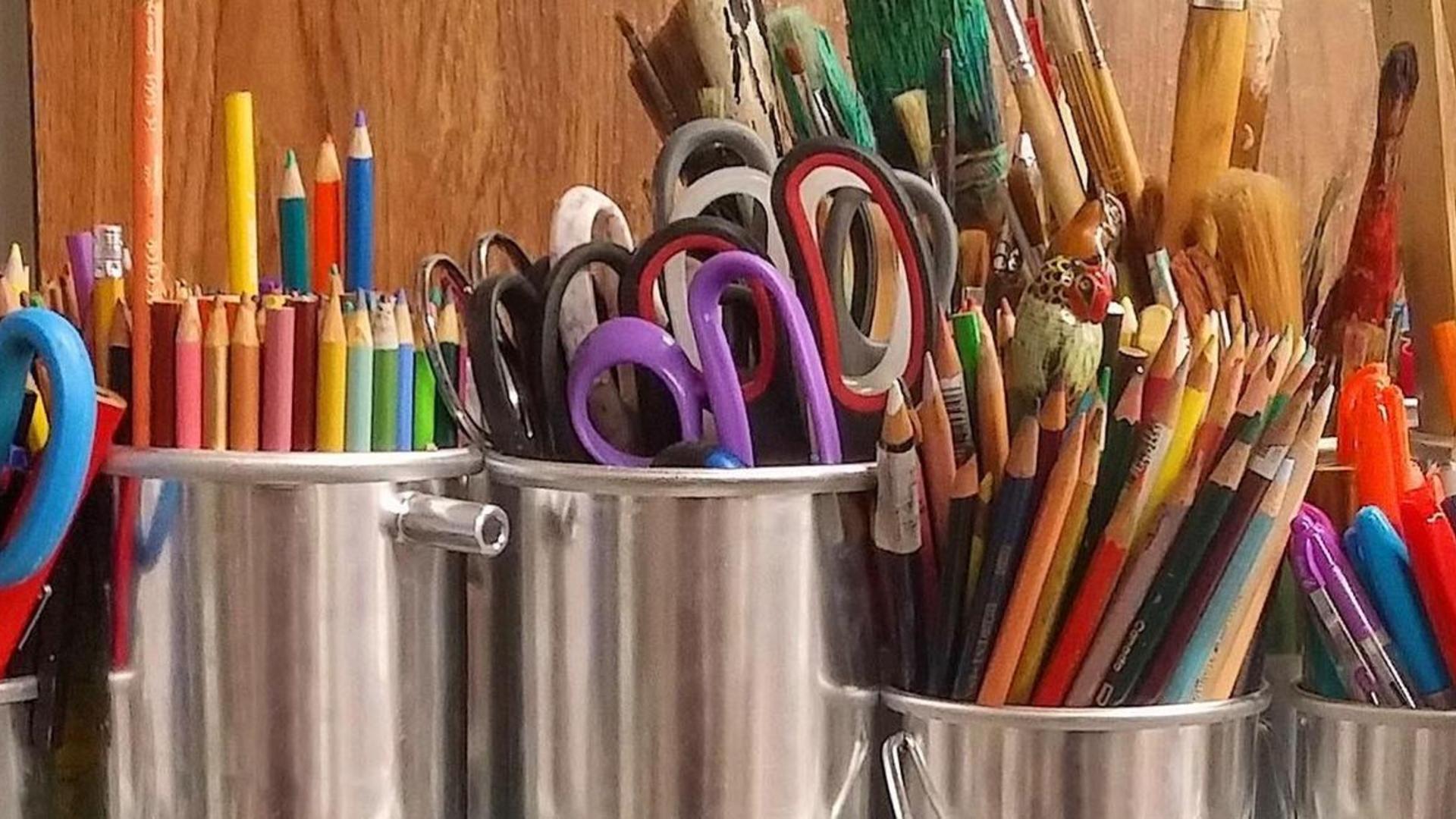 Colorful art supplies including scissors, markers, and pencils in metal containers.