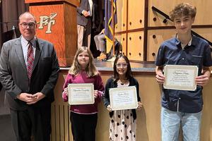 A man and three students holding certificates stand in front of a stage