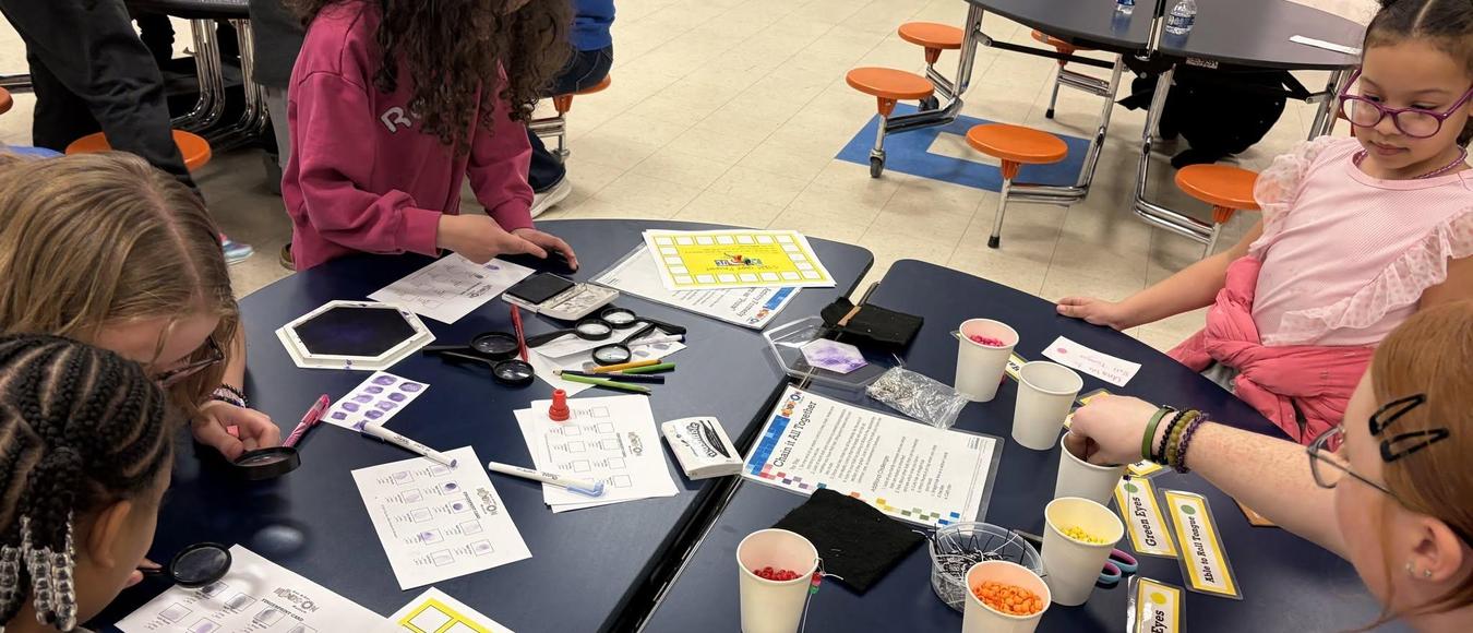 Students fill out STEM Night Passports at a classroom table filled with learning materials.