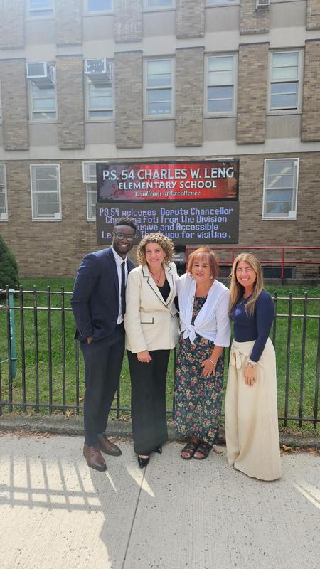 Four educators gathered in front of a school sign, posing for the photo.