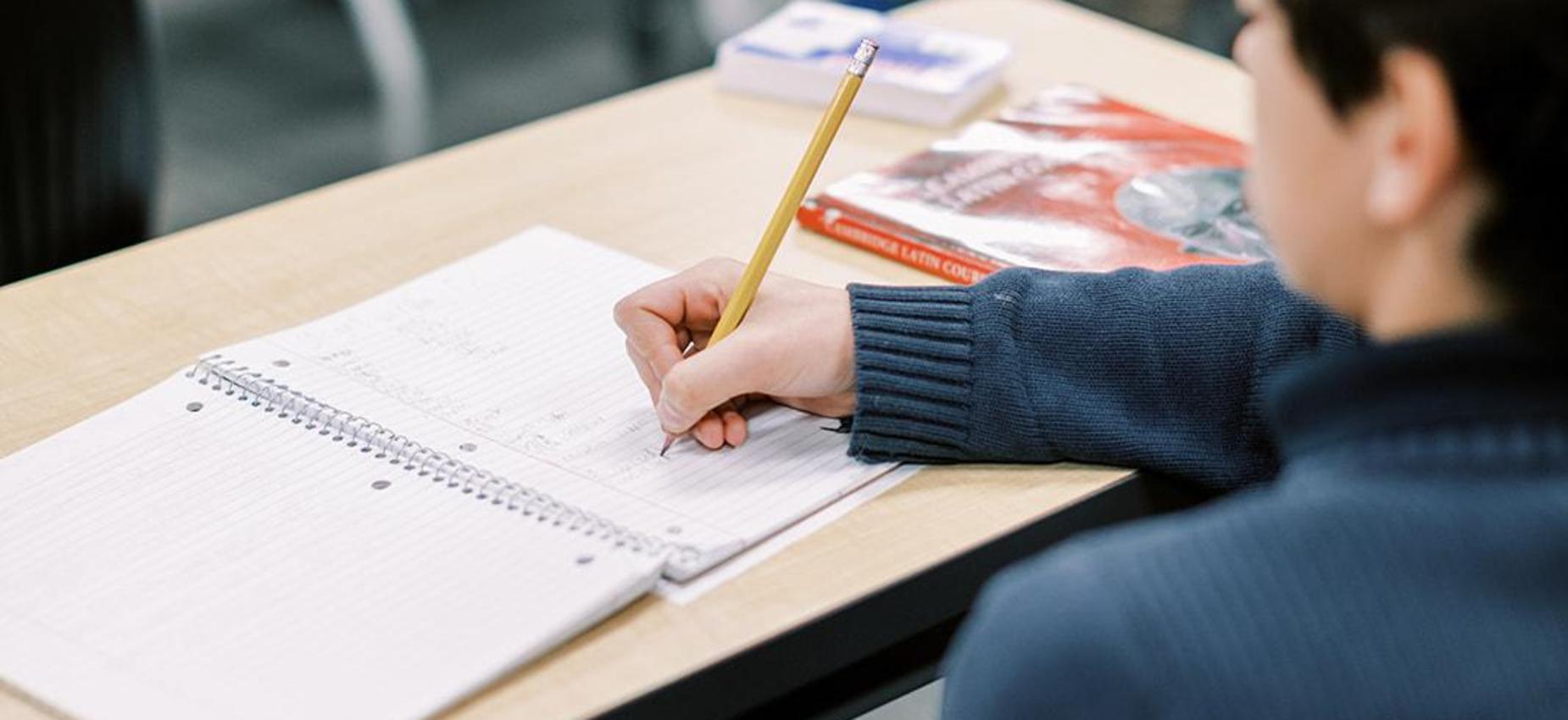 Student writes in a notebook at his desk