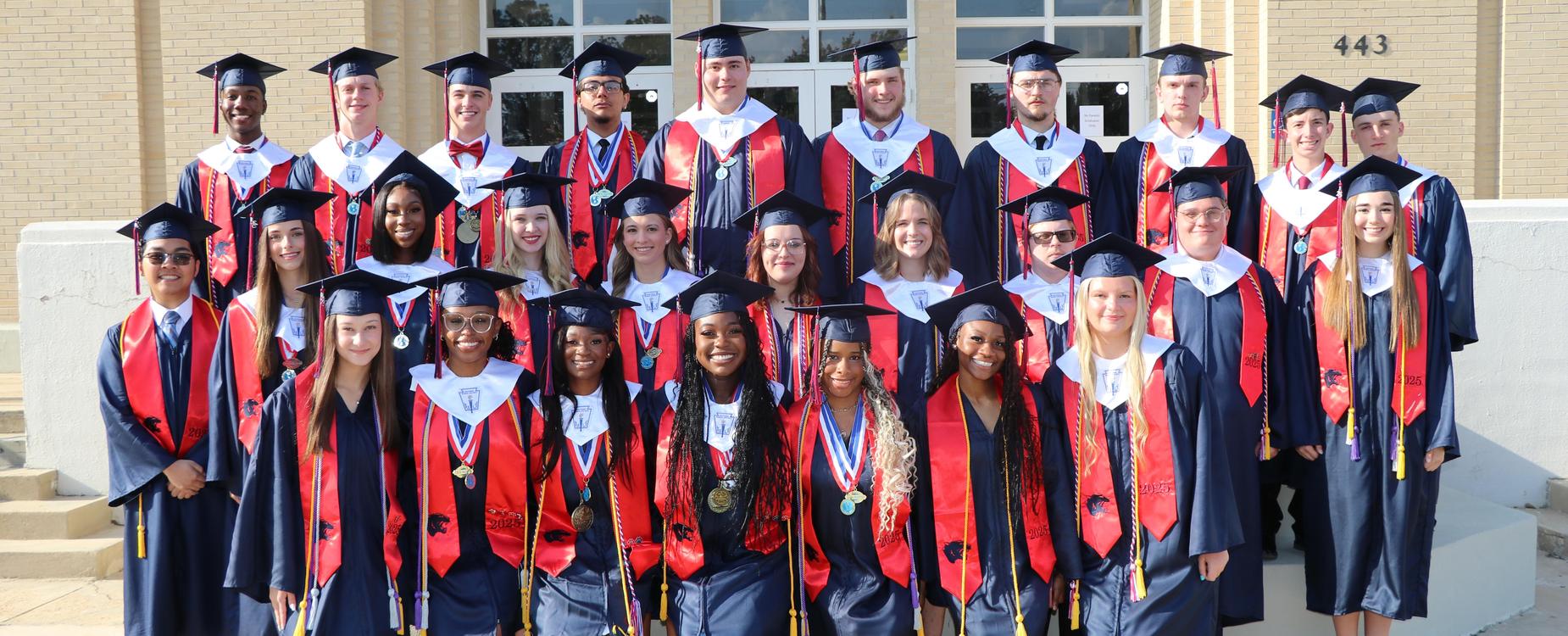 Group of graduates in caps and gowns posing together outside a school building.