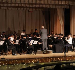 A conductor leads a large band during a performance on stage.