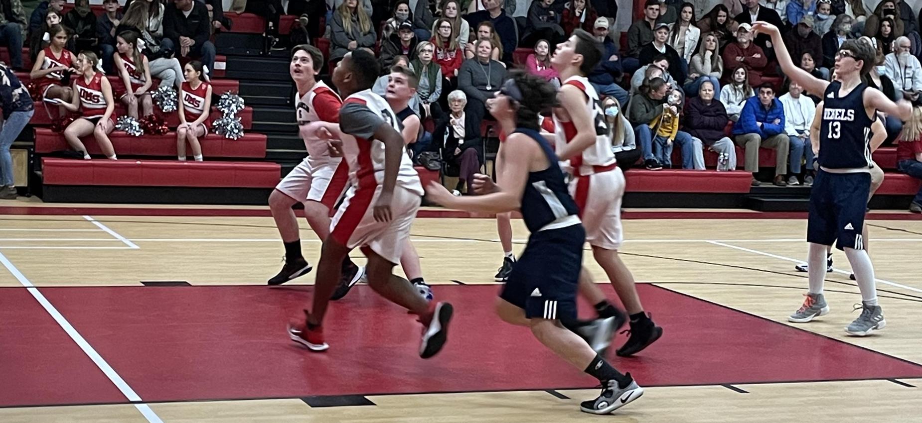 Basketball players wait for a rebound in a gym.