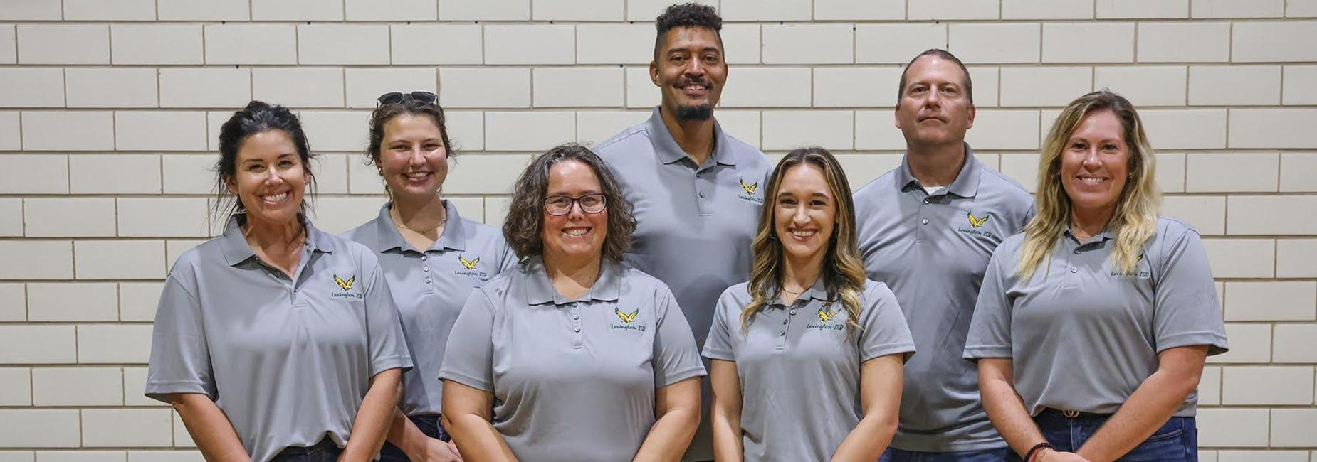 A team of seven staff members in gray shirts, standing together and smiling at the camera.