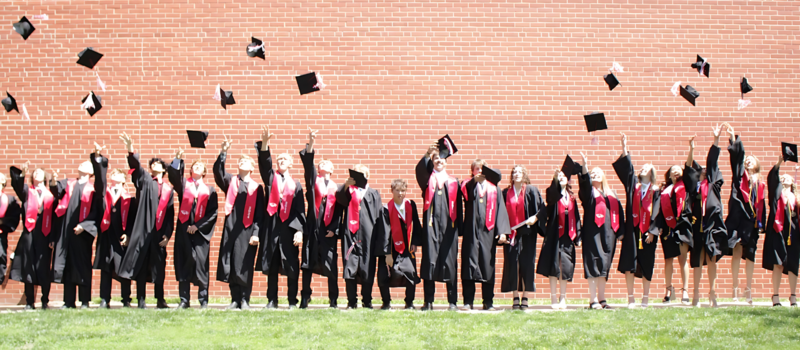 Graduating class throwing caps in the air against a brick wall.