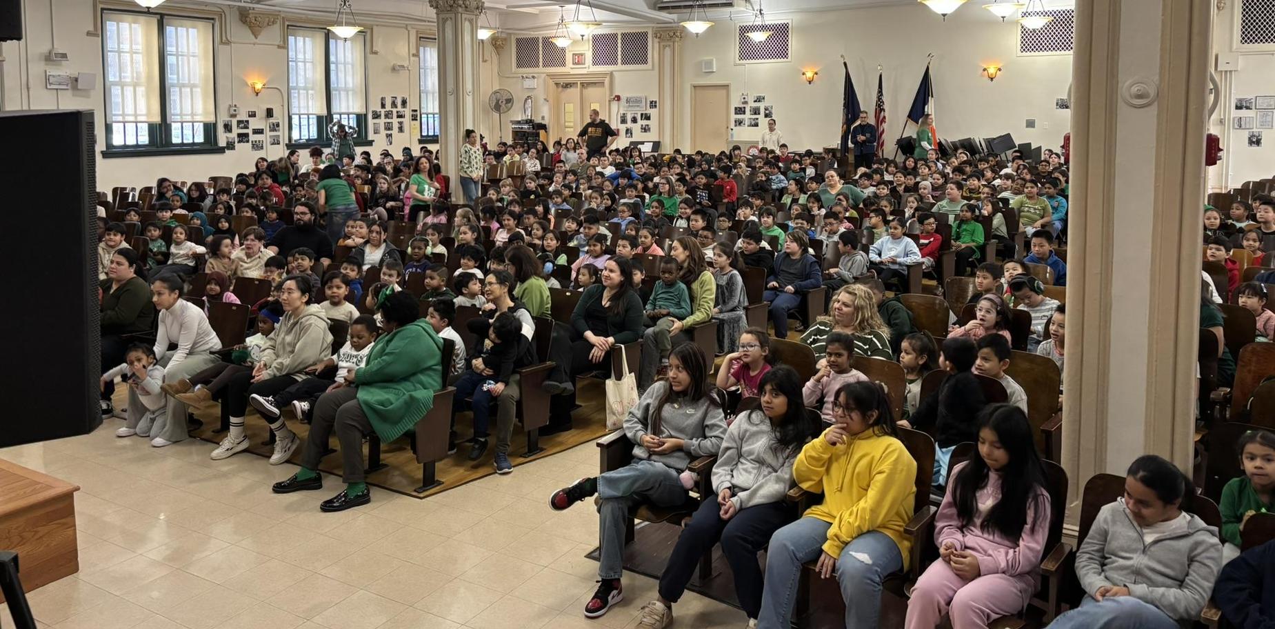 A large audience of children and adults seated in a school auditorium.