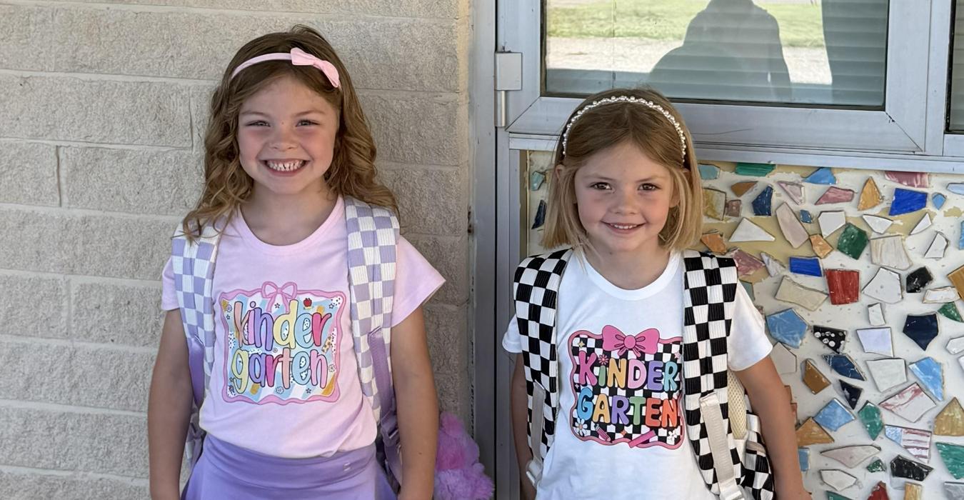 Two girls wearing matching outfits with colorful kindergarten-themed designs.