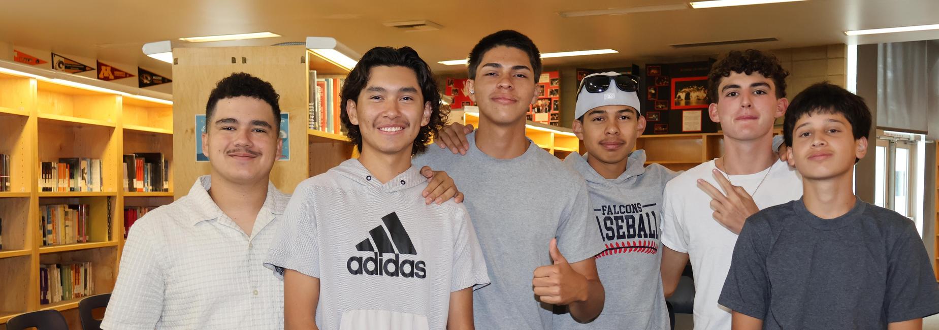 Group of six young men posing together in a library setting.