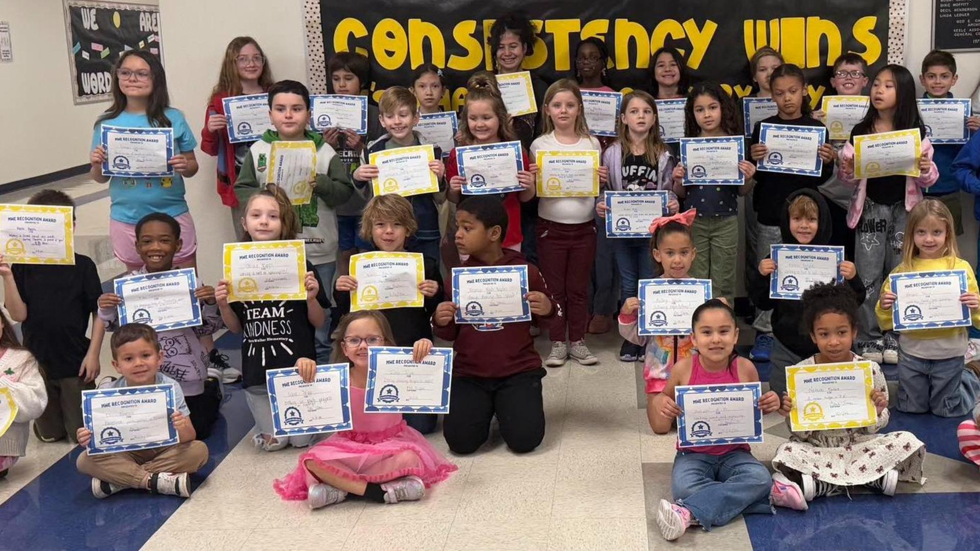 Students holding awards in a school hallway, smiling and posing for the camera.