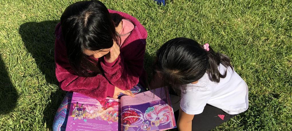 Two students sit together reading a book.