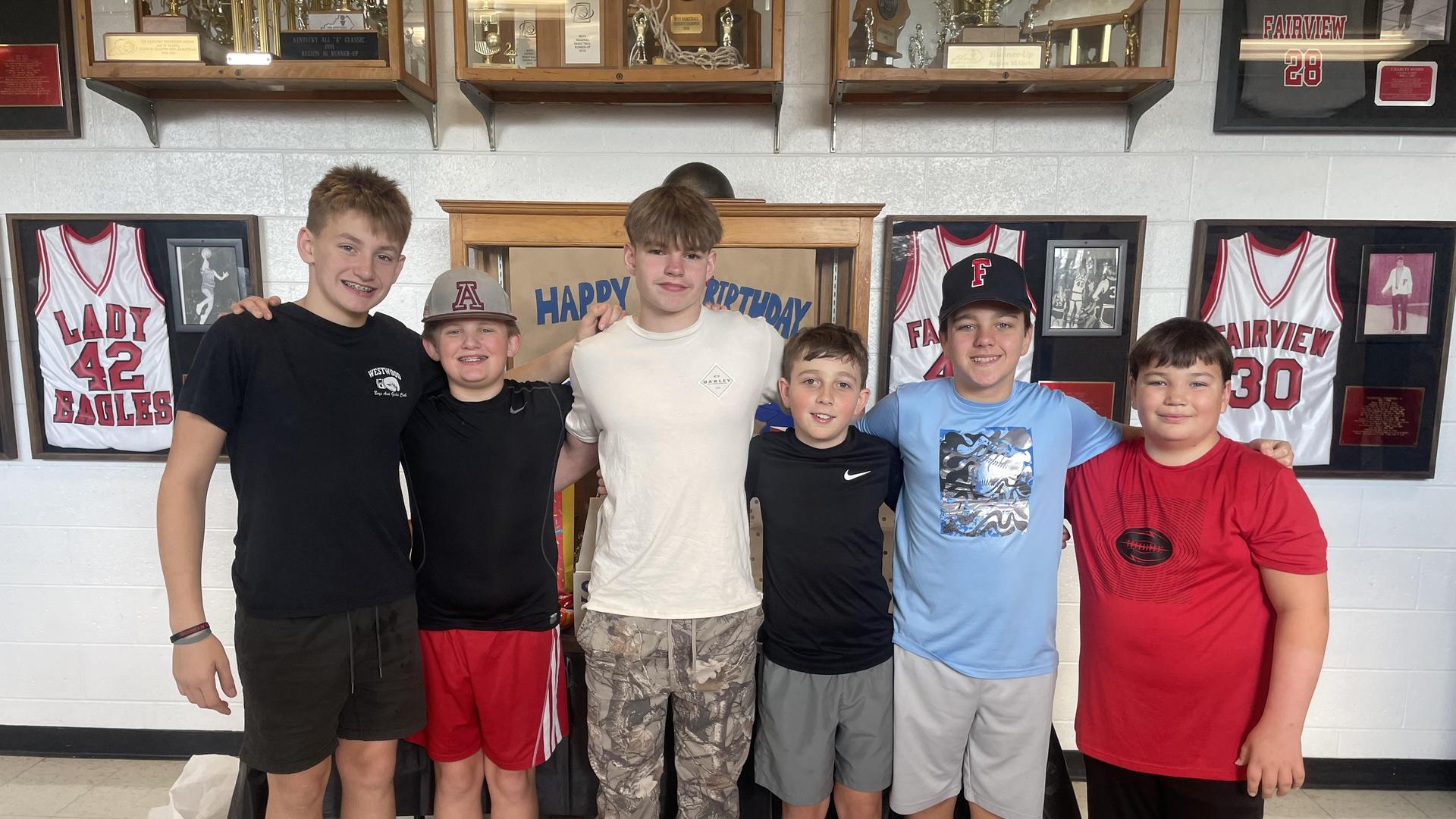 Six boys standing together in a gym, smiling at the camera.