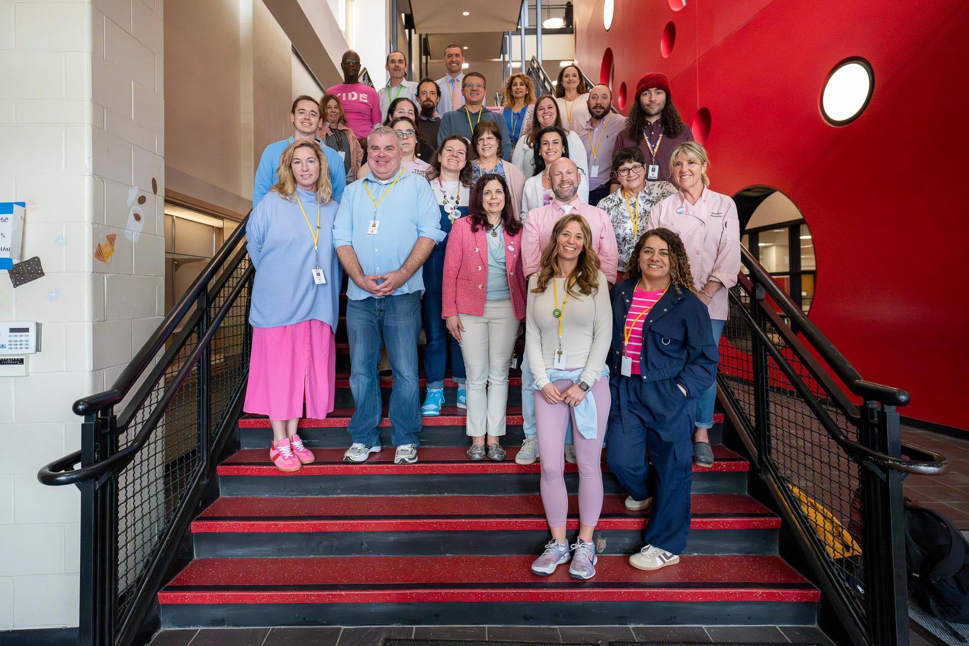 Faculty members standing on stairs in a school, smiling together.